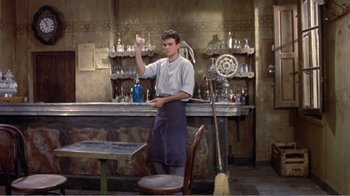Movie still from “Fanny” (1961), directed by Joshua Logan – A man standing in front of a bar holding a glass; Wide shot, Low angle