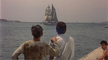 Movie still from “Fanny” (1961), directed by Joshua Logan – Two people look out at a large sail boat in the ocean; Wide shot, High angle