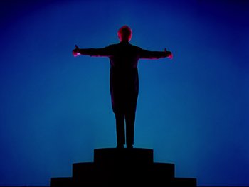 Movie still from “Fantasia” (1940), directed by Ford Beebe Jr. – A man standing on a pedestal with arms outstretched; Wide shot, Low angle