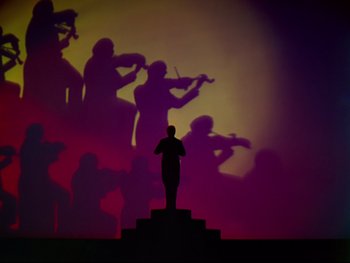 Movie still from “Fantasia” (1940), directed by Ford Beebe Jr. – A silhouette of a person standing in front of a stage with a violin projected on the wall; Extreme Wide shot, Low angle