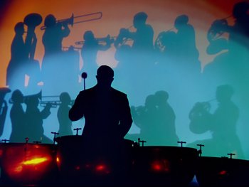 Movie still from “Fantasia” (1940), directed by Ford Beebe Jr. – A silhouette of a man playing drums in front of an audience; Wide shot, Low angle