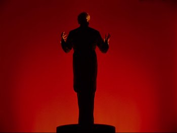 Movie still from “Fantasia” (1940), directed by Ford Beebe Jr. – A man standing in front of a red background; Medium shot, Low angle
