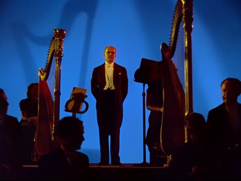 Movie still from “Fantasia” (1940), directed by Ford Beebe Jr. – A man standing on a stage in front of a group of people; Wide shot, Low angle