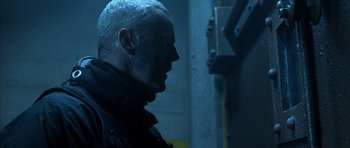 Movie still from “The Rock” (1996), directed by Michael Bay – A man with a shaved head is standing in a dark room; Close Up shot, Low angle