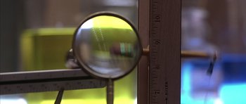 Movie still from “The Rock” (1996), directed by Michael Bay – A magnifying glass and a ruler in a room; Extreme Close Up shot, Low angle