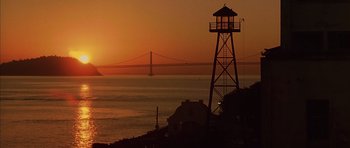 Movie still from “The Rock” (1996), directed by Michael Bay – The sun is setting over the water with a lighthouse in the foreground; Extreme Wide shot, Low angle