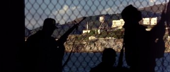 Movie still from “The Rock” (1996), directed by Michael Bay – Two people fishing in front of an island with a water tower in the background; Extreme Wide shot, High angle