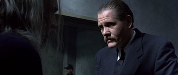 Movie still from “The Rock” (1996), directed by Michael Bay – A man in a suit and tie with a mustache; Close Up shot, Over the shoulder angle