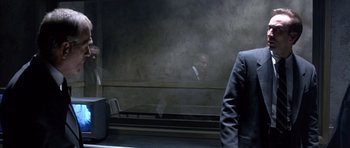 Movie still from “The Rock” (1996), directed by Michael Bay – A man in a suit sitting in front of a window; Medium shot, Over the shoulder angle