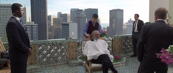 Movie still from “The Rock” (1996), directed by Michael Bay – A man sitting on a chair while a man cuts another man's hair; Wide shot, Low angle