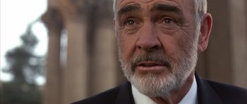 Movie still from “The Rock” (1996), directed by Michael Bay – An older man in a suit and tie looking at the camera; Close Up shot, Low angle
