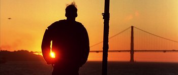Movie still from “The Rock” (1996), directed by Michael Bay – A man standing in front of a bridge at sunset; Wide shot, Low angle