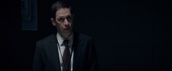 Movie still from “Fantastic Four” (2015), directed by Josh Trank – A man wearing a suit and tie in the dark; Close Up shot, Over the shoulder angle