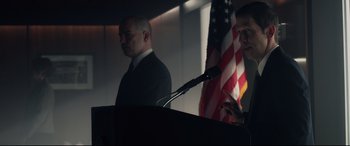 Movie still from “Fantastic Four” (2015), directed by Josh Trank – Two men standing at a podium in front of an american flag; Medium shot, Low angle