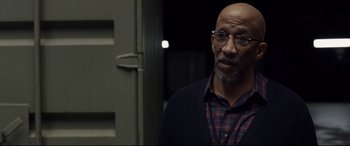 Movie still from “Fantastic Four” (2015), directed by Josh Trank – A bald man with glasses and a plaid shirt is standing in front of a door; Close Up shot, Over the shoulder angle