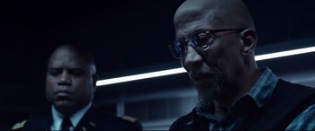 Movie still from “Fantastic Four” (2015), directed by Josh Trank – A man with a bald head wearing glasses; Close Up shot, Over the shoulder angle