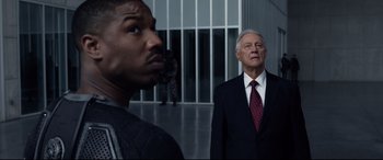 Movie still from “Fantastic Four” (2015), directed by Josh Trank – A man in a suit and tie standing next to another man in a suit and tie; Medium shot, Over the shoulder angle