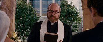 Movie still from “Fantastic Four: Rise of the Silver Surfer” (2007), directed by Tim Story – A man with a beard wearing a priest's outfit holding a bible; Close Up shot, Over the shoulder angle