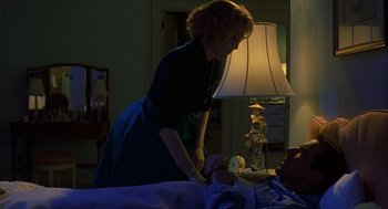 A woman standing next to a man laying in a bed
