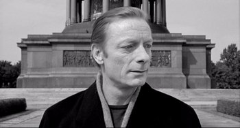 Movie still from “Faraway, So Close!” (1993), directed by Wim Wenders – Black and white photograph of a man in front of a building; Close Up shot, Low angle