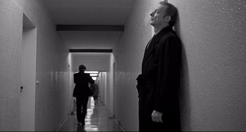 Movie still from “Faraway, So Close!” (1993), directed by Wim Wenders – A black and white photo of a man leaning up against a wall; Wide shot, Low angle