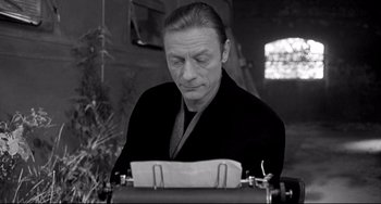 Movie still from “Faraway, So Close!” (1993), directed by Wim Wenders – A man in a black shirt is typing on a typewriter; Close Up shot, High angle