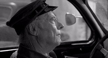 Movie still from “Faraway, So Close!” (1993), directed by Wim Wenders – An old man driving a car in the street; Close Up shot, Over the shoulder angle