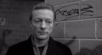 Movie still from “Faraway, So Close!” (1993), directed by Wim Wenders – Black and white photograph of a man in front of a brick wall; Close Up shot, Low angle