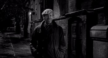 Movie still from “Faraway, So Close!” (1993), directed by Wim Wenders – A black and white photo of a man wearing a hat; Medium shot, Over the shoulder angle
