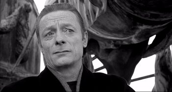 Movie still from “Faraway, So Close!” (1993), directed by Wim Wenders – Black and white photograph of a man in front of a statue; Close Up shot, Low angle