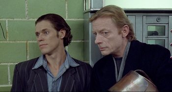 Movie still from “Faraway, So Close!” (1993), directed by Wim Wenders – Two men standing next to each other near a wall; Close Up shot, Low angle