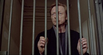 Movie still from “Faraway, So Close!” (1993), directed by Wim Wenders – A man standing behind bars in a jail cell; Close Up shot, Low angle