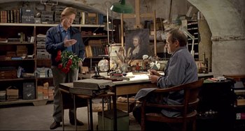 Movie still from “Faraway, So Close!” (1993), directed by Wim Wenders – A man and a woman sitting at a table in front of a painting; Wide shot, High angle