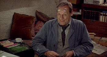 Movie still from “Faraway, So Close!” (1993), directed by Wim Wenders – An older man sitting in a chair wearing glasses; Medium shot, Low angle