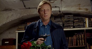 Movie still from “Faraway, So Close!” (1993), directed by Wim Wenders – A man holding a gun in a room with flowers; Medium shot, Over the shoulder angle