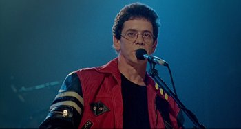 Movie still from “Faraway, So Close!” (1993), directed by Wim Wenders – A man in a red jacket is speaking into a microphone; Close Up shot, Low angle