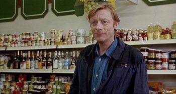 Movie still from “Faraway, So Close!” (1993), directed by Wim Wenders – A man standing in front of shelves filled with food; Medium shot, Over the shoulder angle