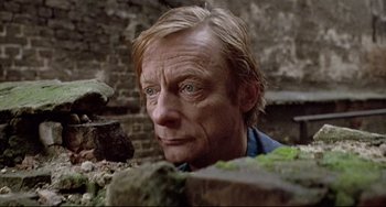 Movie still from “Faraway, So Close!” (1993), directed by Wim Wenders – A person wearing a blue shirt near a brick wall; Close Up shot, Low angle