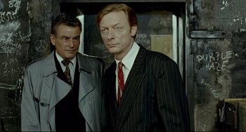 Movie still from “Faraway, So Close!” (1993), directed by Wim Wenders – A man in a suit and tie standing next to another man in a suit and tie; Medium shot, High angle