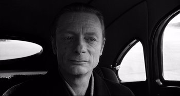 Movie still from “Faraway, So Close!” (1993), directed by Wim Wenders – Black and white photograph of a man in the back of a car; Close Up shot, Over the shoulder angle