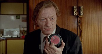 Movie still from “Faraway, So Close!” (1993), directed by Wim Wenders – A man in a black suit holding a container; Close Up shot, Low angle