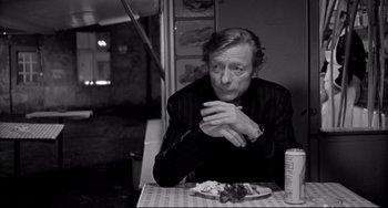 Movie still from “Faraway, So Close!” (1993), directed by Wim Wenders – A man sitting at a table with food in front of him; Medium shot, Over the shoulder angle