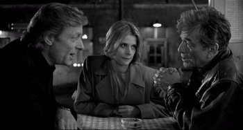Movie still from “Faraway, So Close!” (1993), directed by Wim Wenders – Three people are sitting at a table talking to each other; Medium shot, Over the shoulder angle