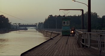 Movie still from “Faraway, So Close!” (1993), directed by Wim Wenders – A person riding a bike on a wooden pier; Extreme Wide shot, High angle