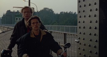 Movie still from “Faraway, So Close!” (1993), directed by Wim Wenders – A man riding a bike next to another man on a bridge; Medium shot, High angle