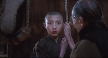 Movie still from “Farewell My Concubine” (1992), directed by Kaige Chen – An older woman is helping a young boy shave his head; Close Up shot, Over the shoulder angle