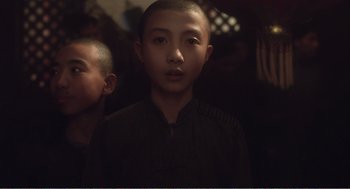 A young boy with a shaved head is looking at the camera