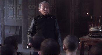 Movie still from “Farewell My Concubine” (1992), directed by Kaige Chen – An older man in a black shirt is talking to some people; Medium shot, High angle