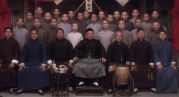Movie still from “Farewell My Concubine” (1992), directed by Kaige Chen – A group of men sitting in front of each other in a room; Wide shot, Low angle