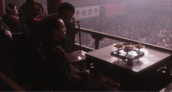 Movie still from “Farewell My Concubine” (1992), directed by Kaige Chen – Two men sitting at a table in front of an audience; Wide shot, High angle